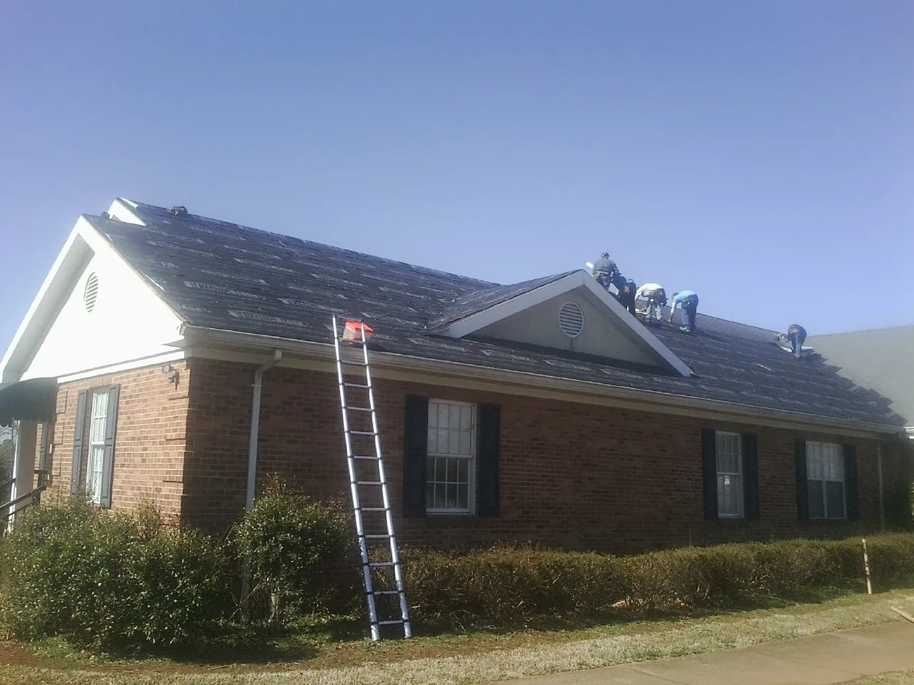 Crew tearing shingles off a brick ranch roof with a ladder set — Emergency Roof Repair work by our crew in Dalmatia