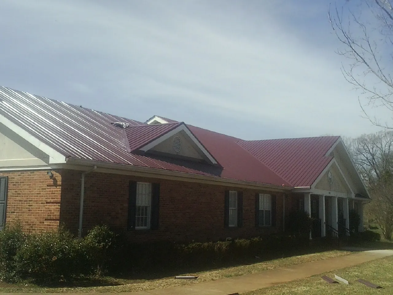 Red metal roof with gabled entries on a long brick building, from a Hail Damage Roof Repair job in Dalmatia